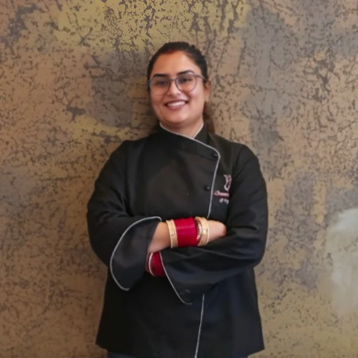 Founder Diksha Dhamija Arora smiling in her black chef coat, standing confidently with folded arms.